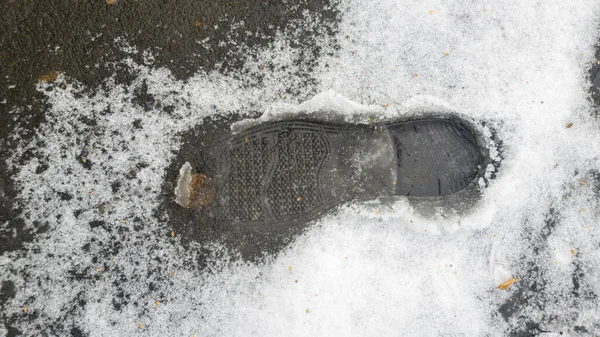 A shoe and boot print on the melted snow, winter. Classic shoe print shape. On the background of yellow leaves and puddles