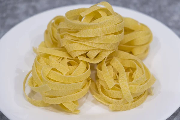Many Italian egg pasta nest on a white plate on a gray background. Soft focus. Motion blur.