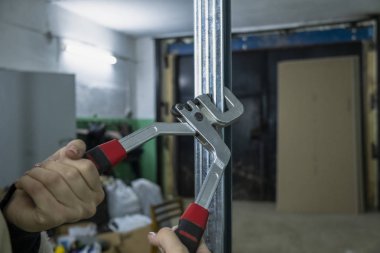 Güzel tırnakları olan bir kadın alçıpan için metal bir profil takmak için özel bir alet kullanır.