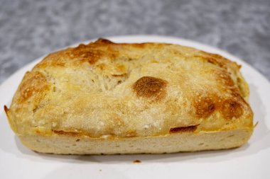 Beyaz bir tabakta gevrek hamurlu ev yapımı ekmek var..