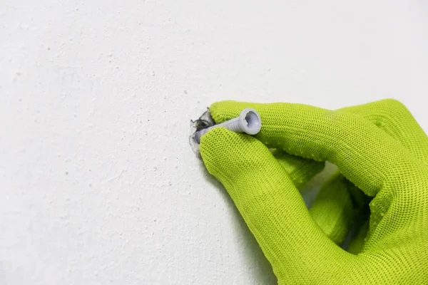 Guante de mano verde trabajador sosteniendo poner en la fachada de plástico blanco tornillo ancla pasador para la construcción de pared . — Foto de Stock