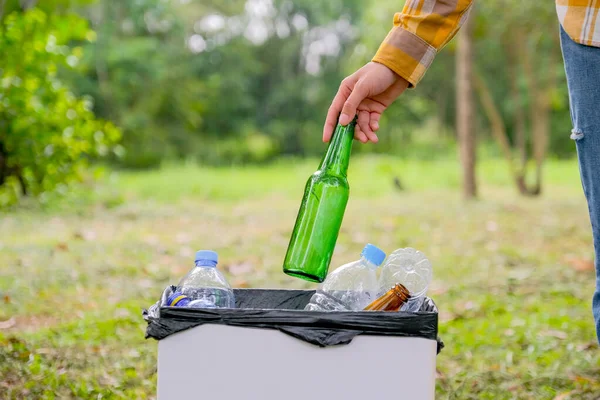 Hands of the women throw the bottle to white bin with disposal bag in the garden with concept of safe environment.