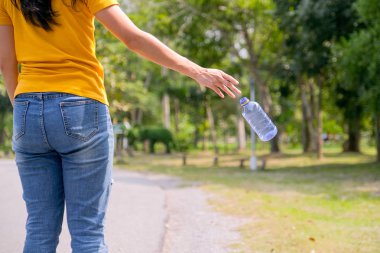 Sarı tişörtlü kadın bahçeye ya da parka plastik şişe fırlatıyor..