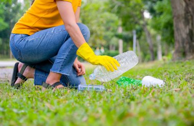 Sarı tişörtlü bir kadının elleri bahçedeki çimlerden çöp toplayarak çevreyi kurtarır..