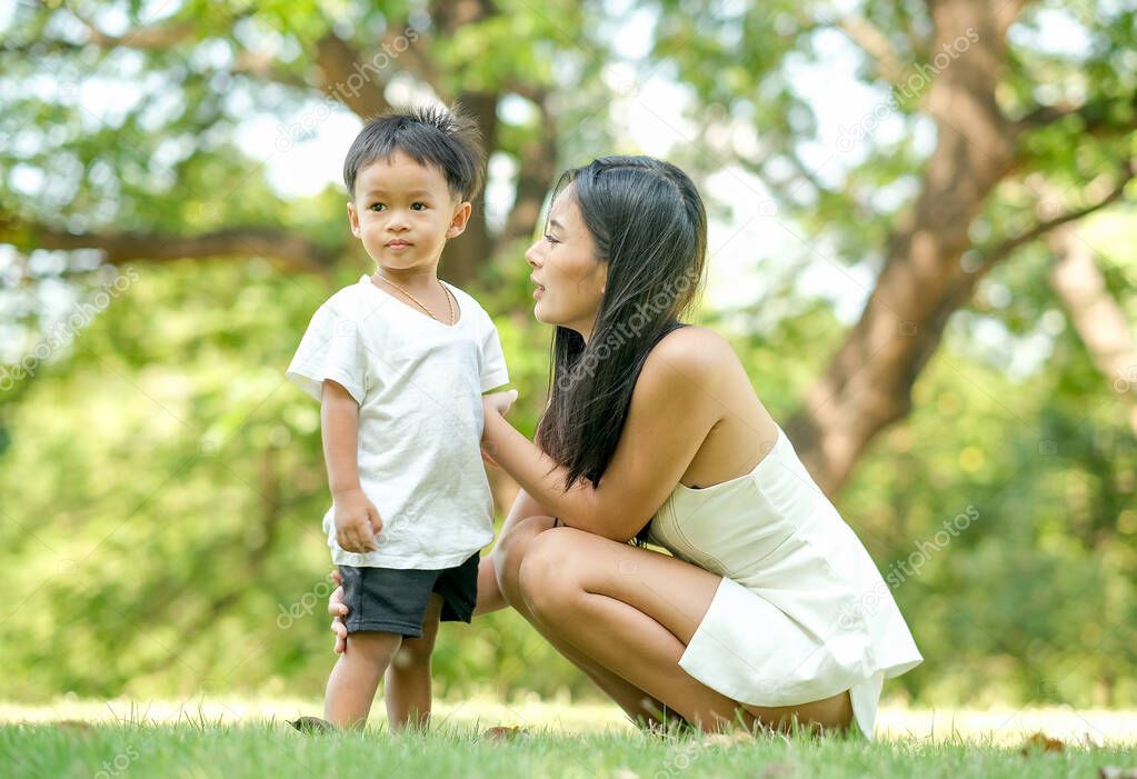 Young Asian mother play and talk with her son in green garden with day light.