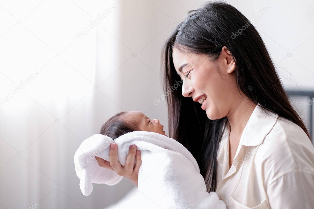 Portrait of young asian mother smile to her newborn baby who look to mother face in the room with white curtain in concept of happy mother and baby.