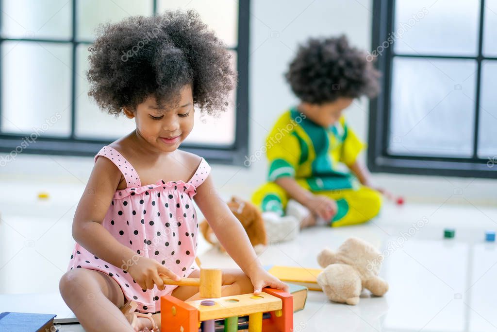 Portrait of one young African mixed race girl is playing with toys in front of the other african boy and look like she enjoy and happy with this activity.