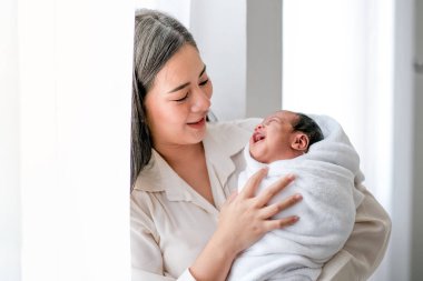 Genç annenin portresi yeni doğan bebeğine bak ve birlikte sabah ışıklarıyla beyaz perdenin önünde gülümsüyorlar..