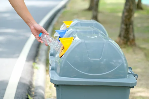 Hand put plastic bottle to the gray bin in park or garden with day light.