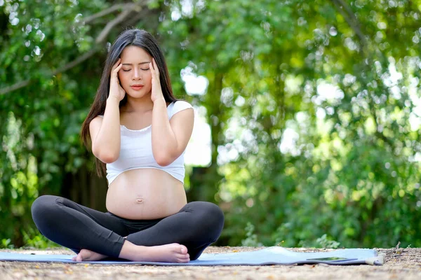 Hamile kadın, bahçede baş ağrısı ya da yoga yaparken park hareketlerini gösteriyor..