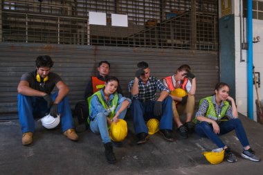 Bir grup teknisyen ya da işçi fabrika kapısının önünde oturup işlerini bitiriyor ve üzgün görünüyorlar..