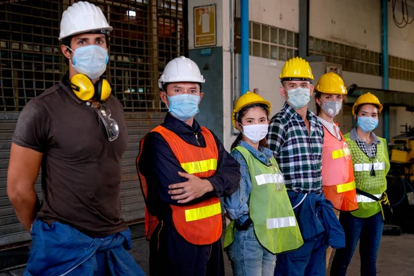 Maskeli bir grup işçi veya teknisyen sağ tarafa bakıp fabrika bölgesinde kalıyorlar..