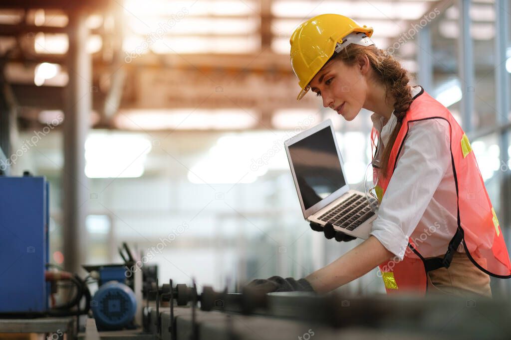 Pretty engineer or technician woman with worker uniform hold laptop computer and check status or maintenance the machine in factory with concept of happiness working for good industrial business.