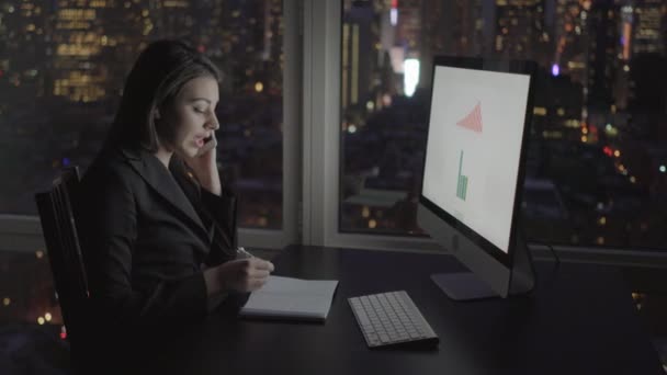 Mujer de negocios trabajando en la computadora y hablando en el teléfono móvil — Vídeo de stock