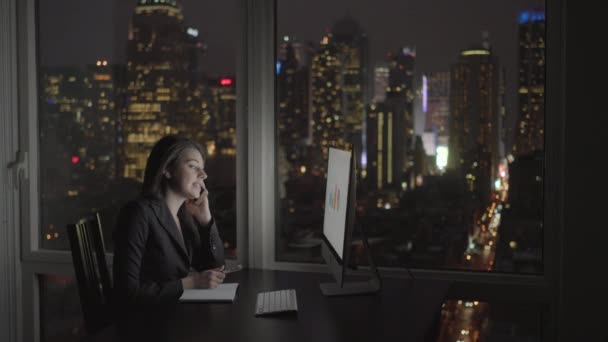 Mujer de negocios trabajando en la computadora y hablando en el teléfono móvil — Vídeo de stock