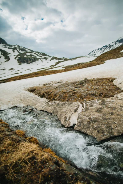 The snow is melting from the mountains and flows in creek, close up. The detailed look at water runs under ice in a river. — Stock Photo, Image