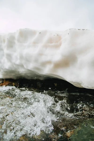 Le regard détaillé sur l'eau coule sous la glace dans une rivière. La neige fond des montagnes et coule dans le ruisseau, gros plan . — Photo