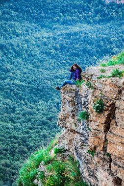 Bir uçurumun üzerinde oturan ve bir manzarayı genç kadın