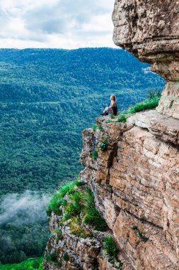 Bir uçurumun üzerinde oturan ve bir manzarayı genç kadın