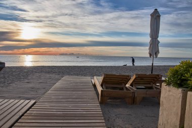 Güneşin doğuşunda güneş şemsiyesi ile plaj şezlongunda