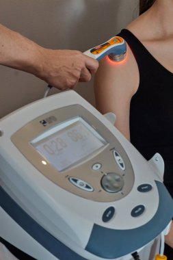 Terapist omzuna ultrason cihazı takıp siyah spor tişörtlü bir kıza jöle veriyor.