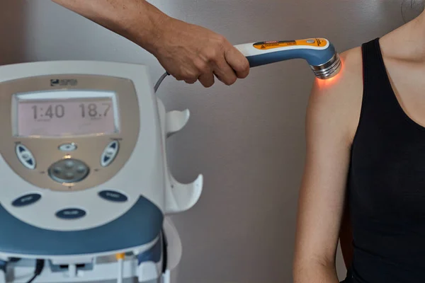 Therapist is applying ultrasound head transducer on the shoulder with gel to a girl with black sport tshirt , Medical equipment use for release pain