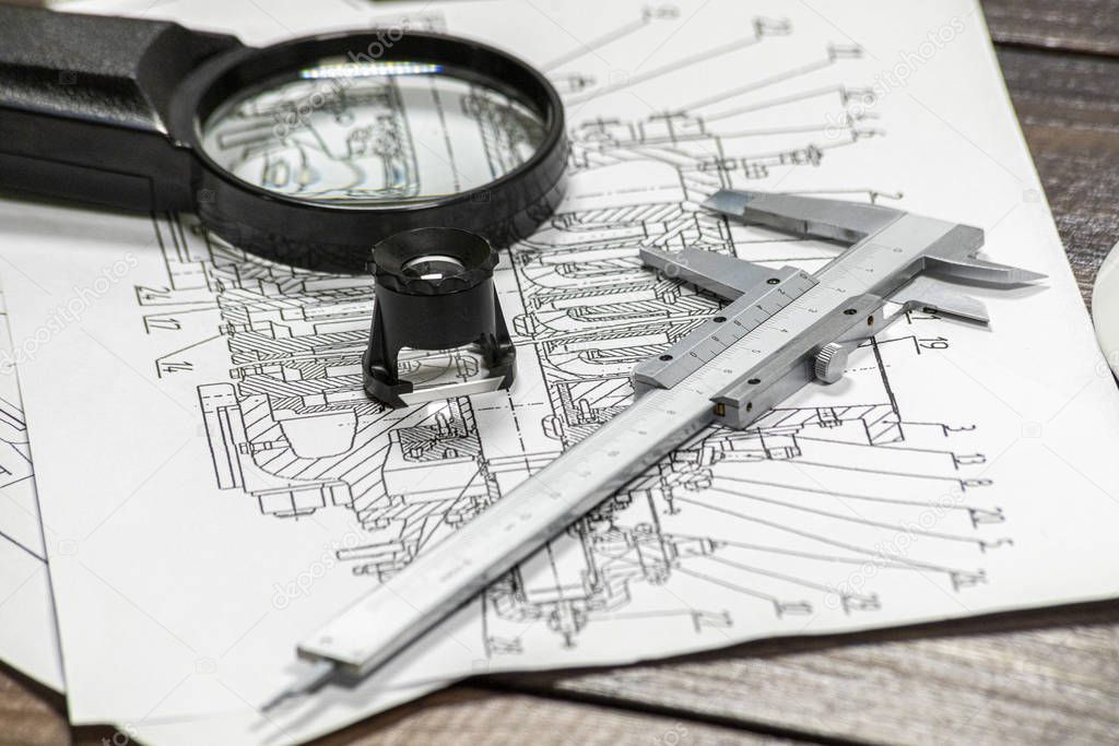 Some pump blueprints on a wooden desk with two magnithing glasses and a calipers. 