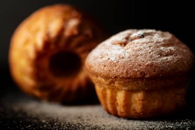 Siyah arka planda pudra şekerli iki fırında kek.