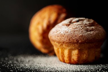 Siyah arka planda pudra şekerli iki fırında kek.