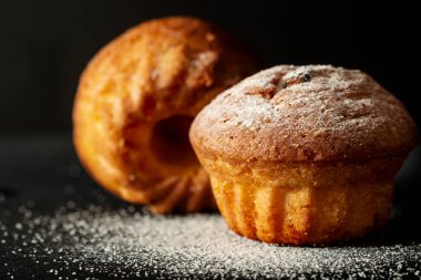 Siyah arka planda pudra şekerli iki fırında kek.