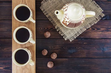 Üç fincan kahve, kahve demliği ve çikolatalı şekerler.