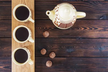 Üç fincan kahve, kahve demliği ve çikolatalı şekerler.