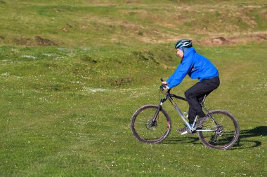 dağ bisikletçinin güneşli güzel bulutlar ile mavi gökyüzüne karşı yeşil orman tepelik kırsal alanda bir toprak yol üzerinde sürme