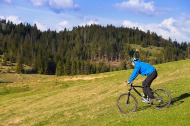 dağ bisikletçinin güneşli güzel bulutlar ile mavi gökyüzüne karşı yeşil orman tepelik kırsal alanda bir toprak yol üzerinde sürme