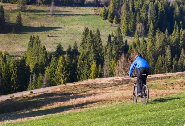 Ciclista de montaña en un día soleado montando en un sinuoso camino de tierra en una zona rural montañosa de bosque verde contra el cielo azul con hermosas nubes — Foto de Stock