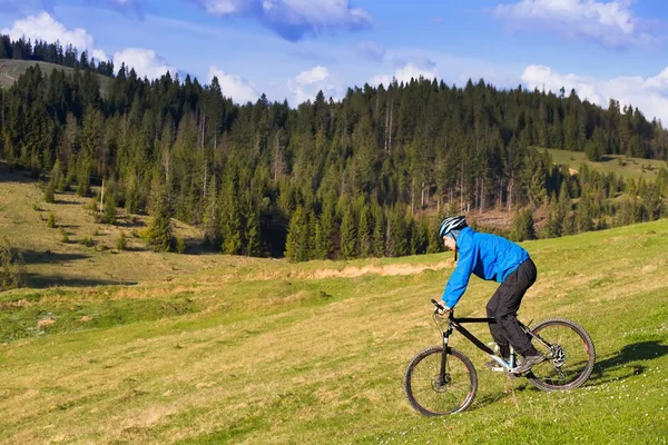 Mountainbiker op zonnige dag rijden op een kronkelende weg van het vuil in een landelijk heuvelachtig gebied van groene bos tegen de blauwe hemel met prachtige wolken — Stockfoto