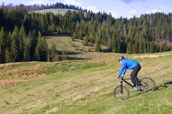 Mountain biker na słoneczny dzień jazda po krętej drodze brudu w wiejskich górzystej okolicy Puszczy zielonej przeciw błękitne niebo z chmurami piękne — Zdjęcie stockowe