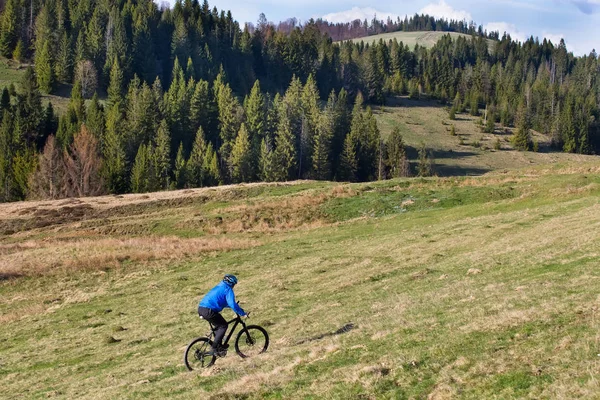 Mountain bike in giornata di sole a cavallo su una strada sterrata tortuosa in una zona collinare rurale di foresta verde contro il cielo blu con belle nuvole — Foto Stock