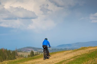 dağ bisikletçinin güneşli güzel bulutlar ile mavi gökyüzüne karşı yeşil orman tepelik kırsal alanda bir toprak yol üzerinde sürme