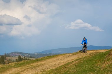 dağ bisikletçinin güneşli güzel bulutlar ile mavi gökyüzüne karşı yeşil orman tepelik kırsal alanda bir toprak yol üzerinde sürme