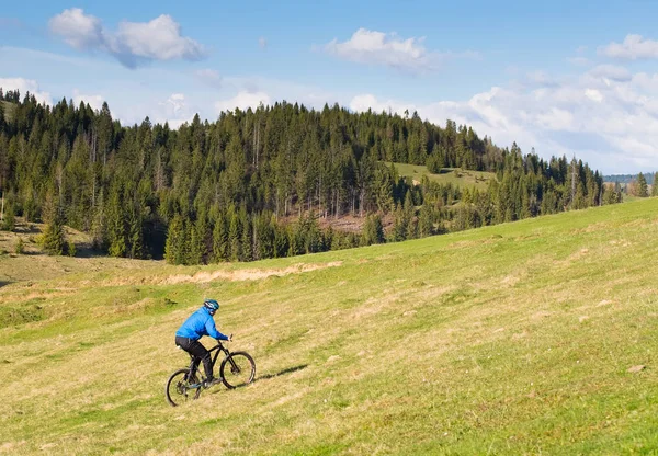 Fjellmotorsyklist på solskinnsdag på en svingete grusvei i et landlig og kupert område med grønn skog mot den blå himmelen med vakre skyer – stockfoto
