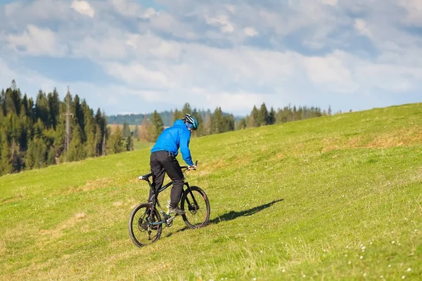 Mountain bike in giornata di sole a cavallo su una strada sterrata tortuosa in una zona collinare rurale di foresta verde contro il cielo blu con belle nuvole — Foto Stock