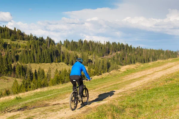 Mountain bike in giornata di sole a cavallo su una strada sterrata tortuosa in una zona collinare rurale di foresta verde contro il cielo blu con belle nuvole — Foto Stock