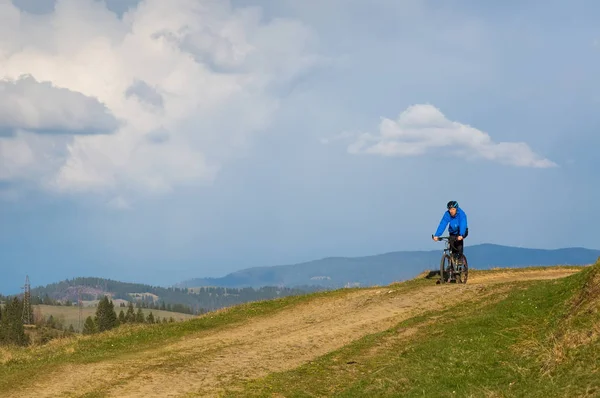 Mountain biker na słoneczny dzień jazda po krętej drodze brudu w wiejskich górzystej okolicy Puszczy zielonej przeciw błękitne niebo z chmurami piękne — Zdjęcie stockowe
