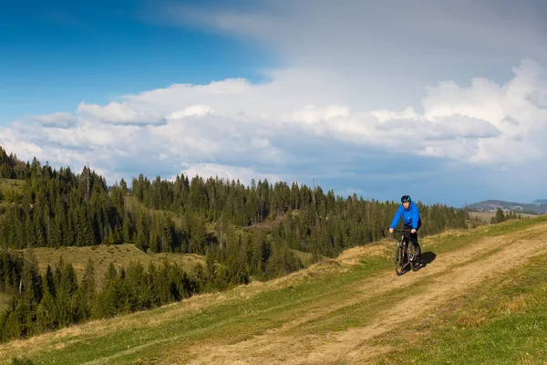 Ciclista de montaña en un día soleado montando en un sinuoso camino de tierra en una zona rural montañosa de bosque verde contra el cielo azul con hermosas nubes —  Fotos de Stock