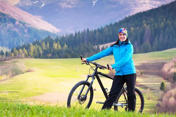 Hermosa chica, ciclista de montaña en soleado día de primavera se encuentra en una zona montañosa en el bosque verde — Foto de Stock