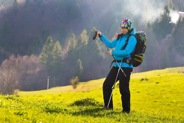 Glückliche junge Frau mit Rucksack und Trekkingstöcken wandert in den Bergen gegen den blauen Himmel mit schönen Wolken. — Stockfoto