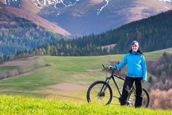 Menina bonita, ciclista de montanha no dia ensolarado da primavera fica em uma área montanhosa na floresta verde — Fotografia de Stock