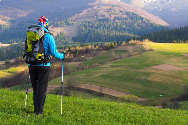 Chica senderista saludable en caminata por la naturaleza. Hermosa joven senderismo feliz se sienta en un prado. Fondo hermosos montes y cielo azul con nubes —  Fotos de Stock