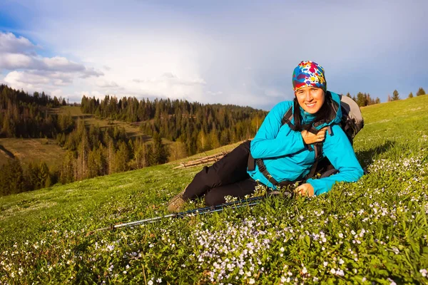 自然ハイキングで健康的なハイカーの少女。幸せなハイキングの美しい若い女性は、草原に座っています。背景の美しい mountayns と雲と青空 — ストック写真